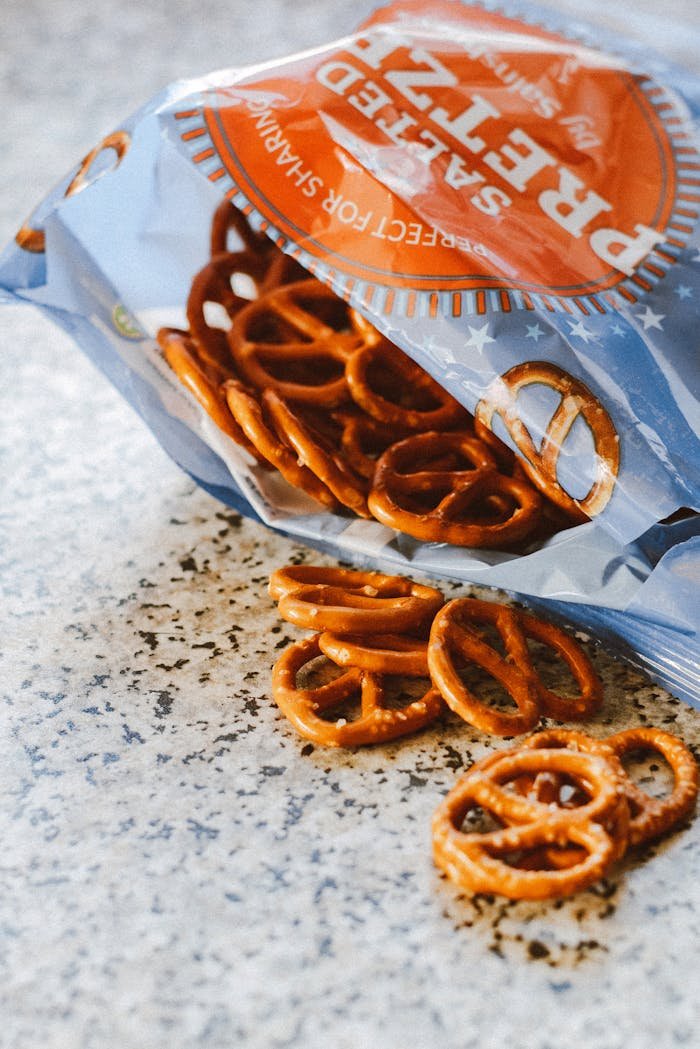 Crispy salted pretzels spilling from an open snack bag on a textured surface.